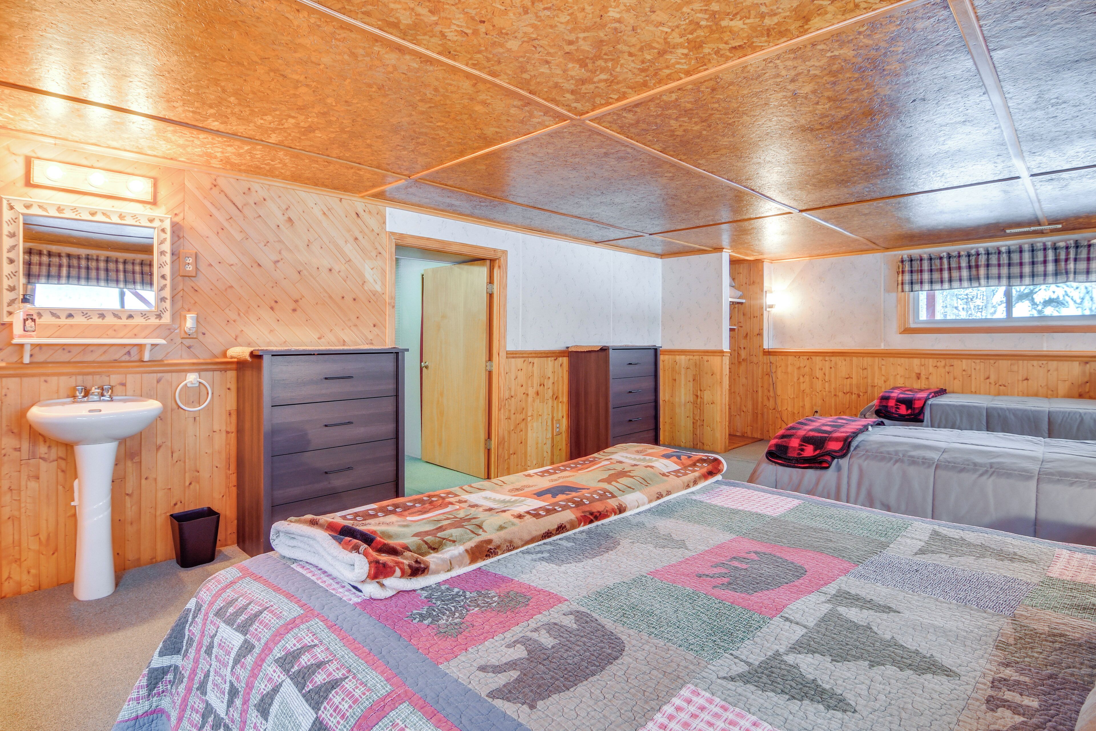 A bedroom with a bed, a bedside table, a mirror, a sink, and a window with a plaid curtain.