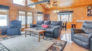 Ein gemütliches Blockhaushaus-Interieur mit Holzbalkendecke, einem grauen Sofa, einem blauen Sessel und einem Essbereich.