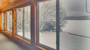 Ein Zimmer mit großen Fenstern, Holzwänden und Blick auf eine verschneite Landschaft.