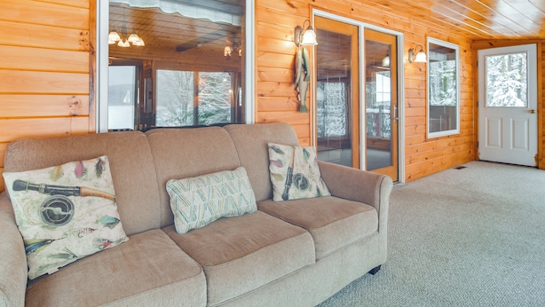 Ein Holzblockhaus-Interieur mit einem beigefarbenen Sofa, zwei Kissen und einer Tür.