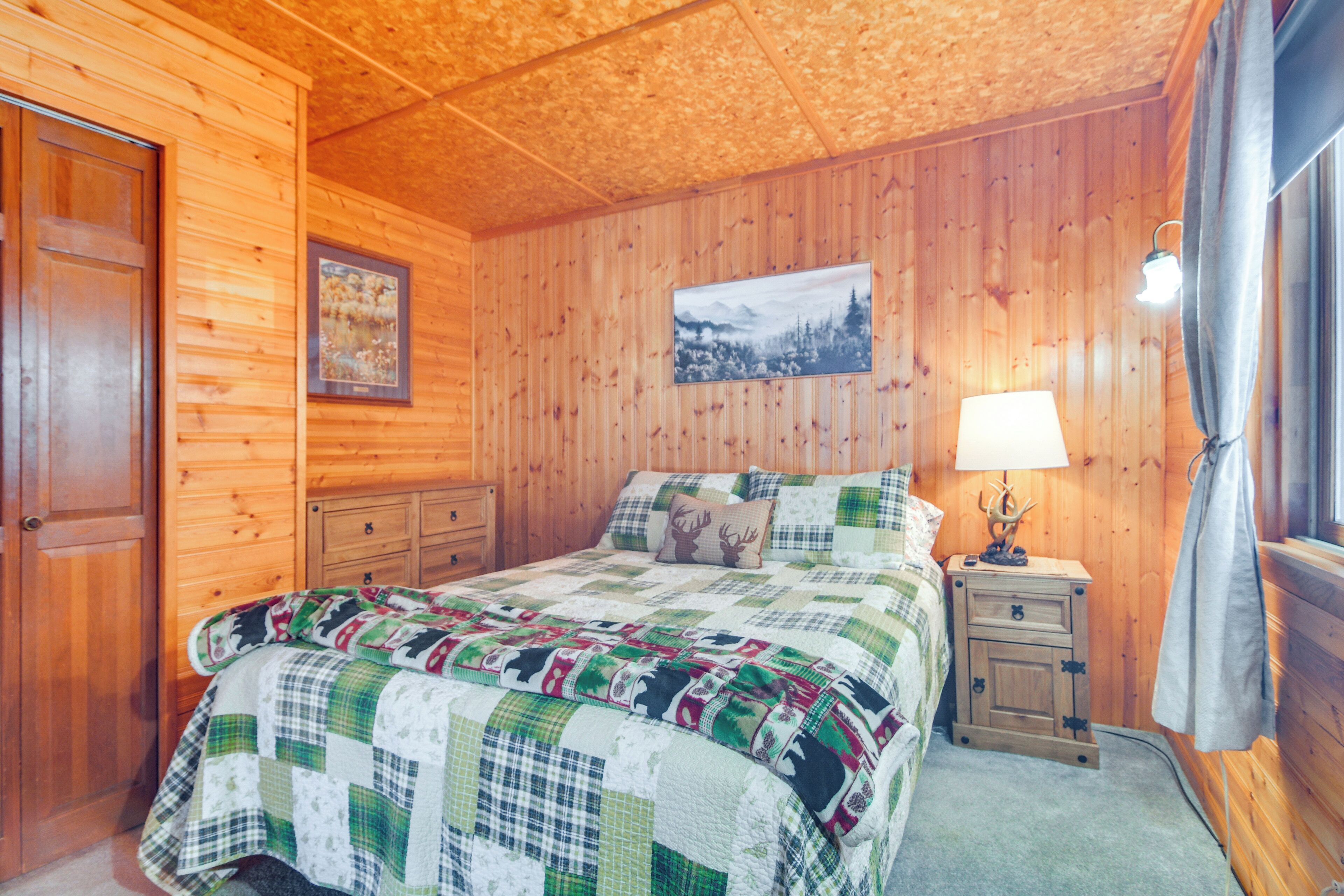 A wooden-paneled bedroom with a bed, a nightstand, a lamp, and a framed picture on the wall.