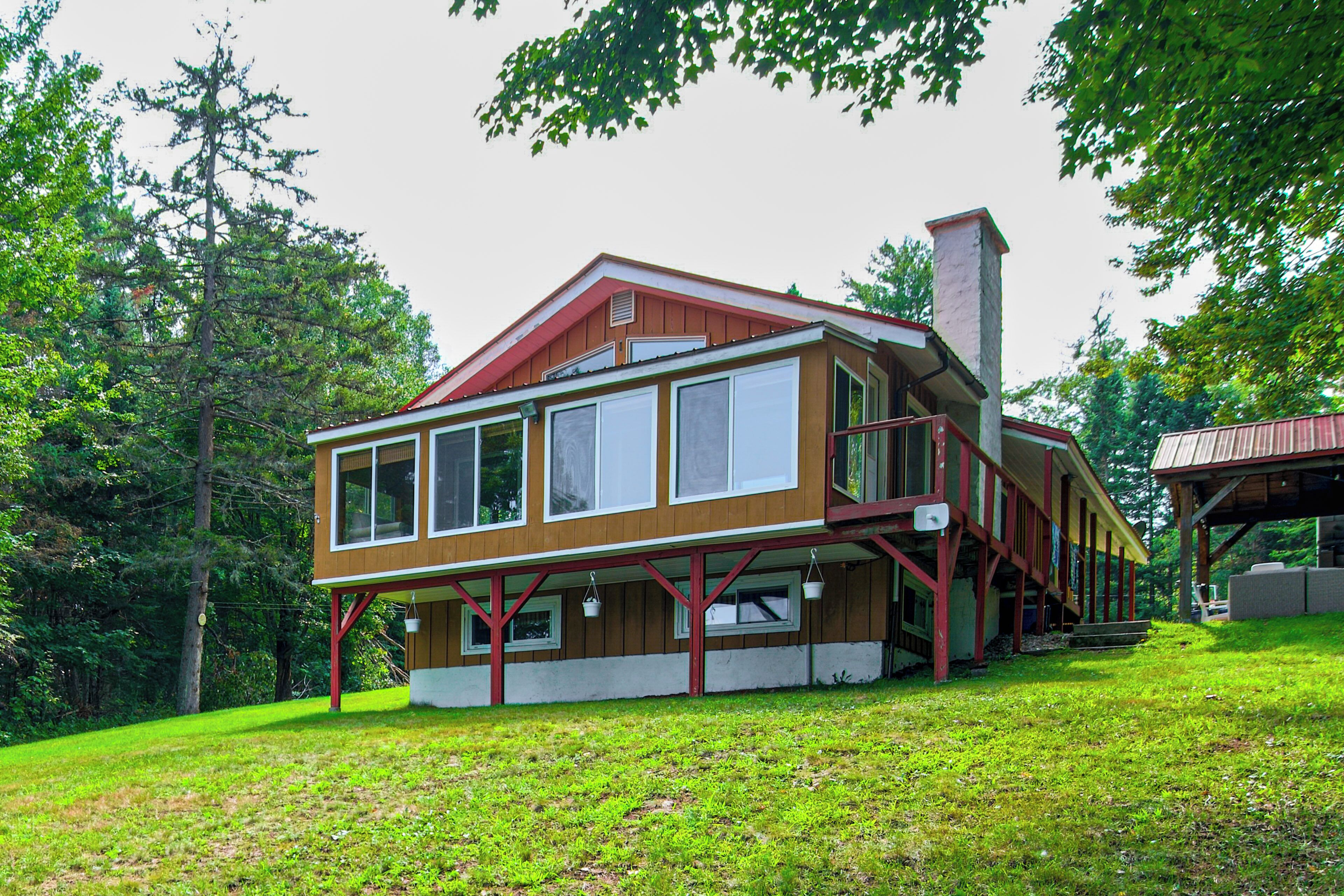 A two-story wooden house with a balcony and a chimney, surrounded by trees.