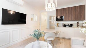Een moderne keuken met een flatscreen-tv, houten kasten en een eethoek met een marmeren tafel en stoelen.
