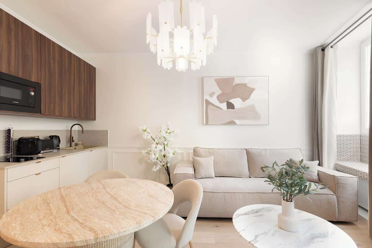 A modern living room with a round marble coffee table, a beige sofa, and a chandelier.
