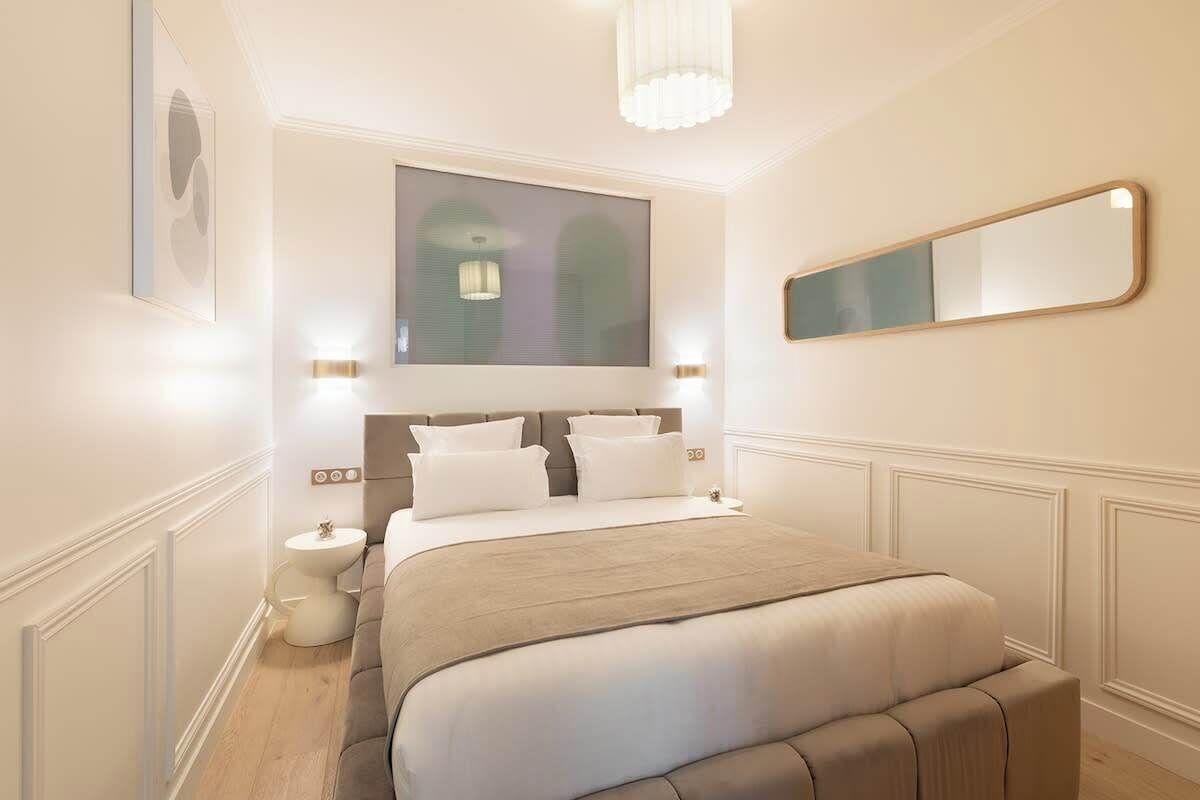 Un dormitorio moderno con una cama grande, lámparas de noche, un espejo y un candelabro.