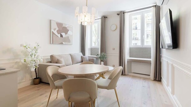 Een moderne eetruimte met een ronde tafel, beigekleurige stoelen en een kroonluchter.