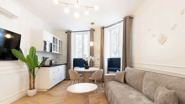 A modern living room with a sofa, a round coffee table, and a dining area with a table and chairs. - A Sublime 1-BR with Services in Batignolles (Paris)
