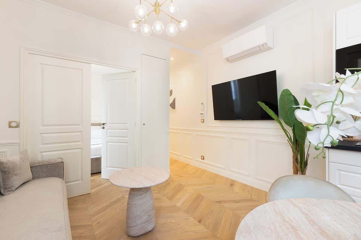 A modern living room with a sofa, a round table, and a TV mounted on the wall.