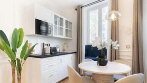 A modern kitchen with white cabinets, a black microwave, and a dining area with a round table and chairs. - A Sublime 1-BR with Services in Batignolles (Paris)