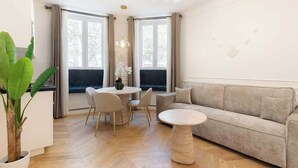 A modern living room with a sofa, a round coffee table, a dining table with chairs, and a large plant. - A Sublime 1-BR with Services in Batignolles (Paris)