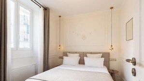 A hotel room with a large bed, a small bedside table, a mirror, and a window with curtains. - A Sublime 1-BR with Services in Batignolles (Paris)