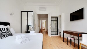 A hotel room with a large bed, a desk, a chair, and a TV mounted on the wall.