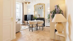 A well-lit living room with a television, a round table with chairs, a large mirror, and a decorative lamp.