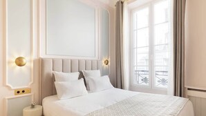 A hotel room with a large bed, a nightstand, a wall-mounted light, and a window with curtains.