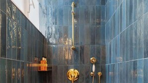 A shower with a gold showerhead and a handheld showerhead, set against dark blue tiles.