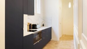 A modern kitchen with dark cabinetry, a white countertop, and a window above the sink.