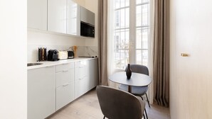 A modern kitchen with white cabinets, a microwave, and a coffee machine. There is a round table with a chair and a vase.