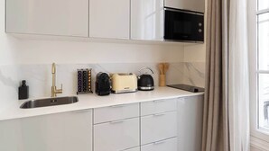 A modern kitchen with white cabinets, a stainless steel sink, a black microwave, a toaster, and a kettle.