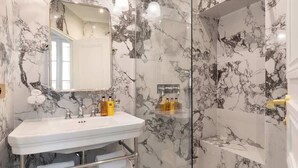 A bathroom with a marble sink, a glass shower enclosure, and a mirror.