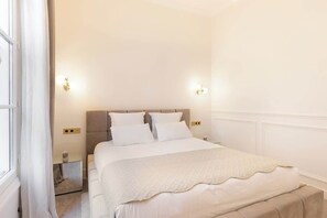 A neatly arranged bedroom with a bed, bedside tables, and wall-mounted lighting. - A Distinguished Studio with Services in Opera (Paris)