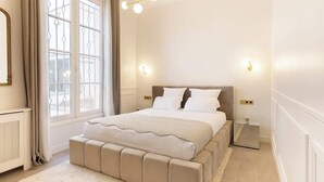 A bedroom with a large bed, a bedside table, a mirror, and a window with curtains.