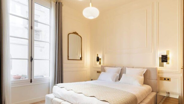 A bedroom with a large bed, a mirror, and two wall-mounted lights. - A Romantic Studio with Services in Opera (Paris)