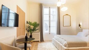 A modern hotel room with a bed, a round table with chairs, a potted plant, and a large window with curtains. - A Romantic Studio with Services in Opera (Paris)