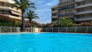 A swimming pool surrounded by a fence, with palm trees and flowering plants. - Le balcon de Funès, 4min walk from the beach, with swimming pool, parking, 70m2 7personnes (Fréjus)