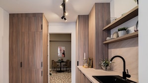 A modern kitchen with wooden cabinetry, a black sink, and a dining area visible in the background. - Loggia Luxe 5BR Living in Universitatii Area (Bucharest)
