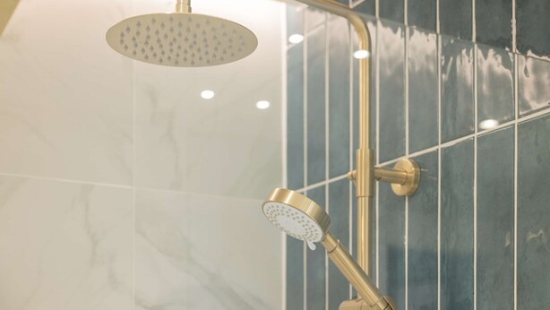 Une douche équipée d’un pommeau de douche à main et d’un pommeau de douche fixé au mur, dans une salle de bain dont les murs sont recouverts de carreaux.