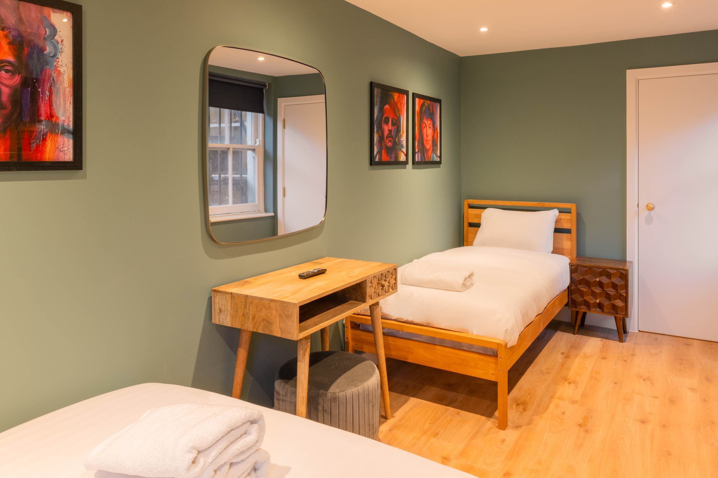 A bedroom with a wooden bed, a bedside table, a mirror, and a window.