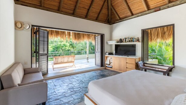 Un dormitorio con una cama grande, un televisor y un balcón con techo de paja.
