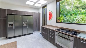 Una cocina moderna con armarios oscuros, electrodomésticos de acero inoxidable y un amplio ventanal con vistas a un jardín exuberante.