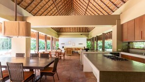 A spacious dining area with a large table and chairs, a kitchen with a modern design, and a thatched roof ceiling. - Atonishing 5BR Villa at Mesa de Yeguas (Anapoima)