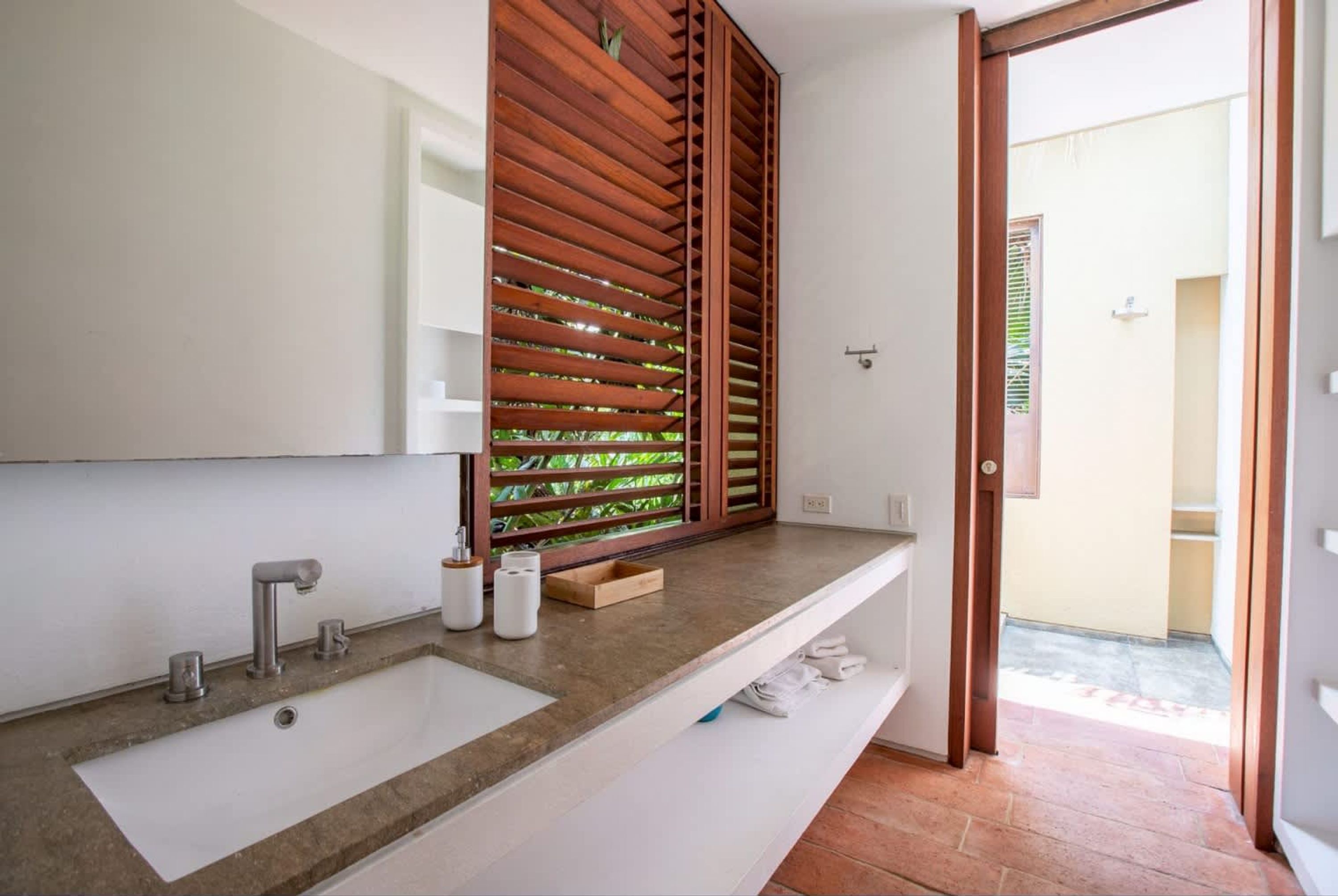 A modern bathroom with a large sink, a mirror, and wooden blinds.