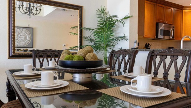 Una mesa de comedor dispuesta con tazas y platos blancos, un cuenco con alimentos esféricos, y un espejo encima.