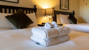 Habitación de hotel con dos camas, ropa blanca y una pila de toallas dobladas sobre la cama.