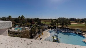 Un resort con una gran piscina, palmeras y un campo de golf al fondo.
