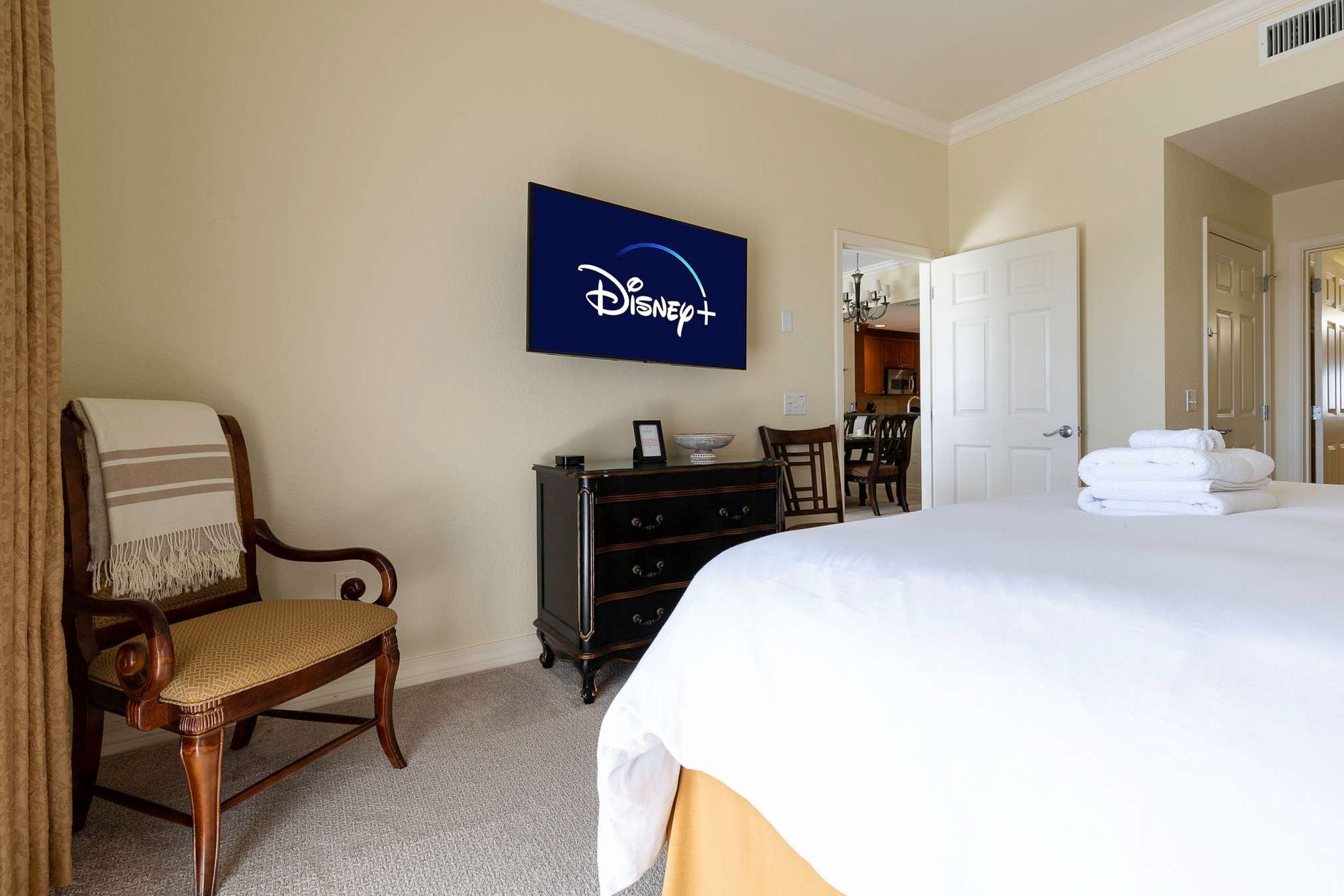 Et hotelværelse med en seng, en stol, en kommode og et Disney+-skilt på væggen.