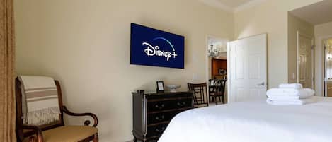 Et hotelværelse med en seng, en stol, en kommode og et Disney+-skilt på væggen.