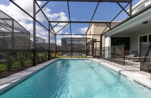 A swimming pool with a glass enclosure, surrounded by a patio area with lounge chairs and a view of neighboring houses. - Family Friendly 5BR Home Pool Patio Room for 10 (Clermont)