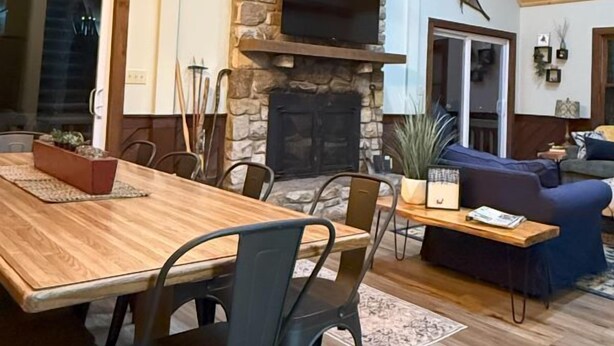 Un salón amplio con chimenea de piedra, vigas de madera en el techo y una gran mesa de comedor.