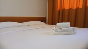 Een opgemaakt bed met witte lakens en een stapel handdoeken ernaast.