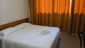 Een hotelkamer met een opgemaakt bed, een houten hoofdbord en oranje gordijnen.