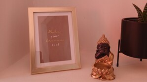 Een lijst met een inspirerende quote aan de muur, een klein Boeddhabeeldje en een kamerplant.