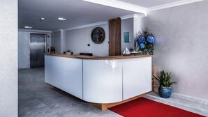 Un área de recepción con un mostrador de madera, un reloj, un cuadro enmarco y una planta en maceta.