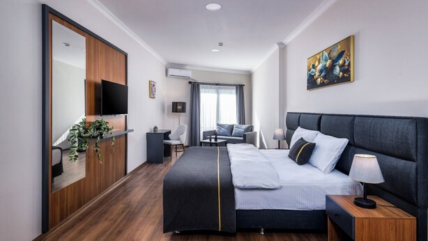 Una habitación de hotel moderna con una cama grande, un escritorio, una silla, un televisor y un cuadro en la pared.