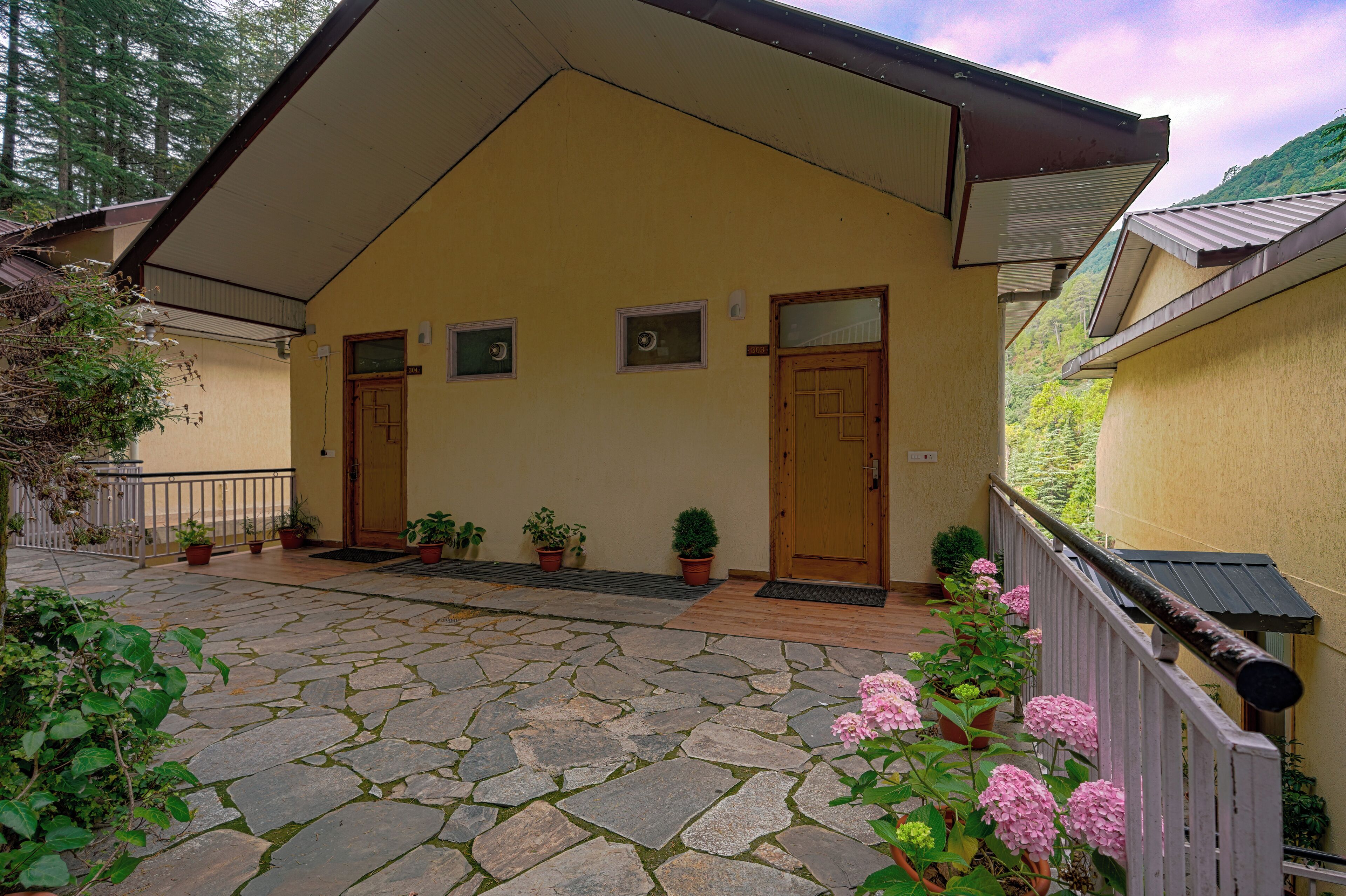 A yellow building with two doors, a stone-paved entrance, and potted plants.