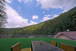 Una terrazza con erba sintetica, mobili in legno e vista su una montagna boscosa.