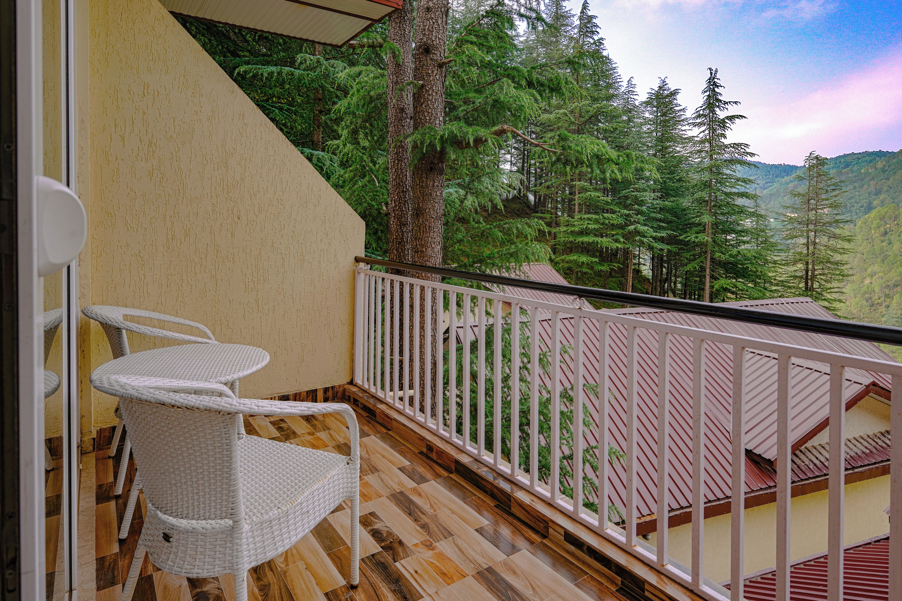 Un balcon avec des fauteuils en osier blanc, un plancher en bois et une vue sur une montagne boisée.